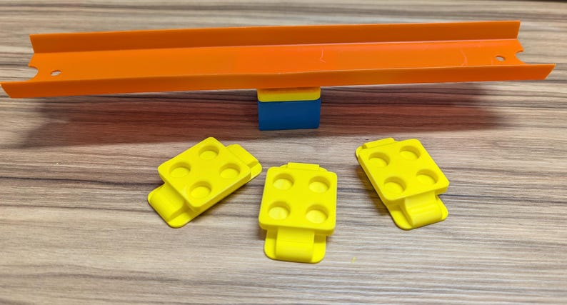 Peut inclure: Trois pi&egrave;ces de piste en plastique jaune avec six trous chacune, con&ccedil;ues pour un ensemble de piste de course pour enfants. Les pi&egrave;ces sont sur une surface en bois, avec une pi&egrave;ce de piste orange vif.