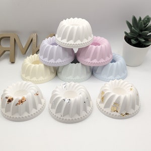 Peut inclure: Un ensemble de huit petits bougeoirs en forme de g&acirc;teau, de couleur blanche. Certains sont blancs unis, tandis que d'autres ont des accents de feuilles d'or ou d'argent. Les bougeoirs sont dispos&eacute;s en forme de pyramide.