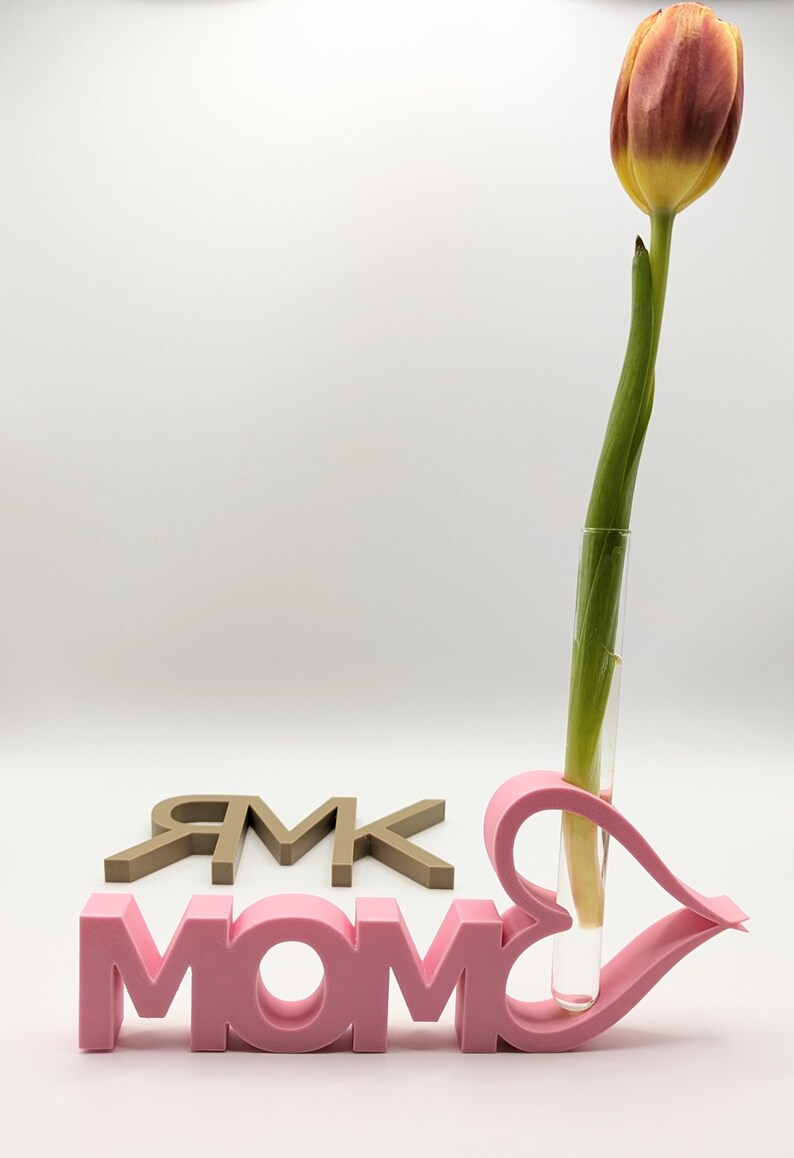 Pu&ograve; includere: Segno 3D MOM rosa con un vaso a forma di cuore che contiene un solo tulipano arancione e giallo.