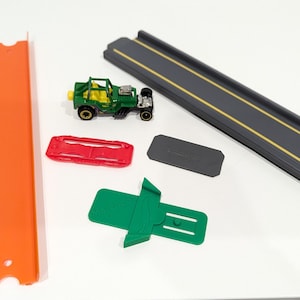 Peut inclure: Une voiture jouet verte avec des roues noires et un circuit de jeu rouge, orange et noir. Le circuit comprend une voie droite, une voie courbe et une rampe.
