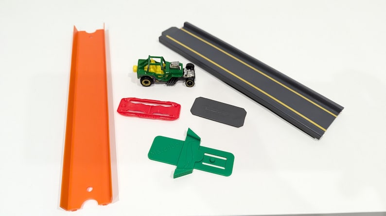 Peut inclure: Une voiture jouet verte avec des roues noires et un circuit de jeu rouge, orange et noir. Le circuit comprend une voie droite, une voie courbe et une rampe.