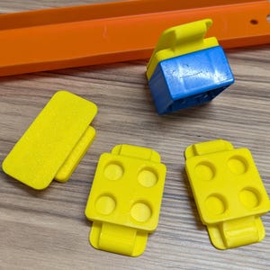 Peut inclure: Quatre pi&egrave;ces de piste en plastique jaune pour un circuit de voitures miniatures. Trois pi&egrave;ces ont quatre trous chacune et une pi&egrave;ce est un rectangle plat. Il y a aussi une pi&egrave;ce de connexion en plastique bleu.