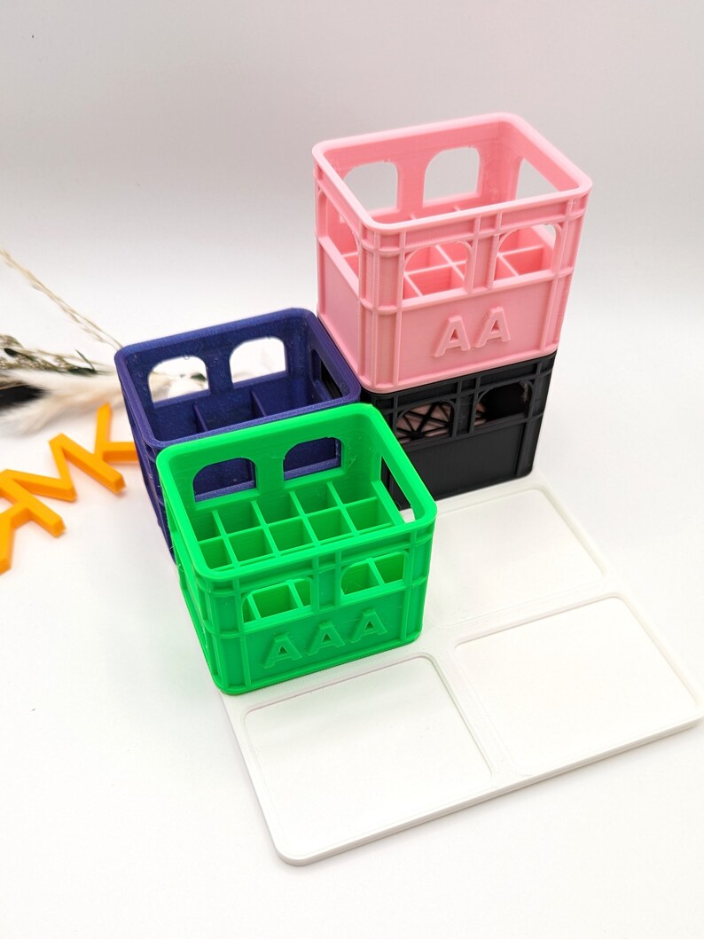 Op de afbeelding: Een stapel kleurrijke miniatuurkratten in roze, blauw en groen, met een wit dienblad. Op de roze krat staat "AA". Op de groene krat staat "AAA". De kratten zijn op elkaar gestapeld.