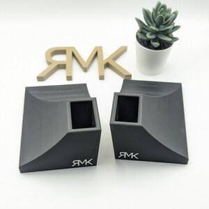 Puede incluir: Dos rampas de skate de pl&aacute;stico negro con un recorte cuadrado en el centro. Las rampas tienen un borde curvo y la palabra "RMK" est&aacute; impresa en la parte inferior de cada rampa.