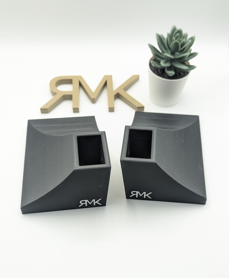 Puede incluir: Dos rampas de skate de pl&aacute;stico negro con un recorte cuadrado en el centro. Las rampas tienen un borde curvo y la palabra "RMK" est&aacute; impresa en la parte inferior de cada rampa.