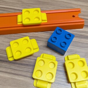 Peut inclure: Quatre pi&egrave;ces en plastique jaune avec quatre trous chacune et un bloc en plastique bleu avec quatre trous. Les pi&egrave;ces jaunes ont une rainure sur le c&ocirc;t&eacute; et sont con&ccedil;ues pour se connecter &agrave; une piste.