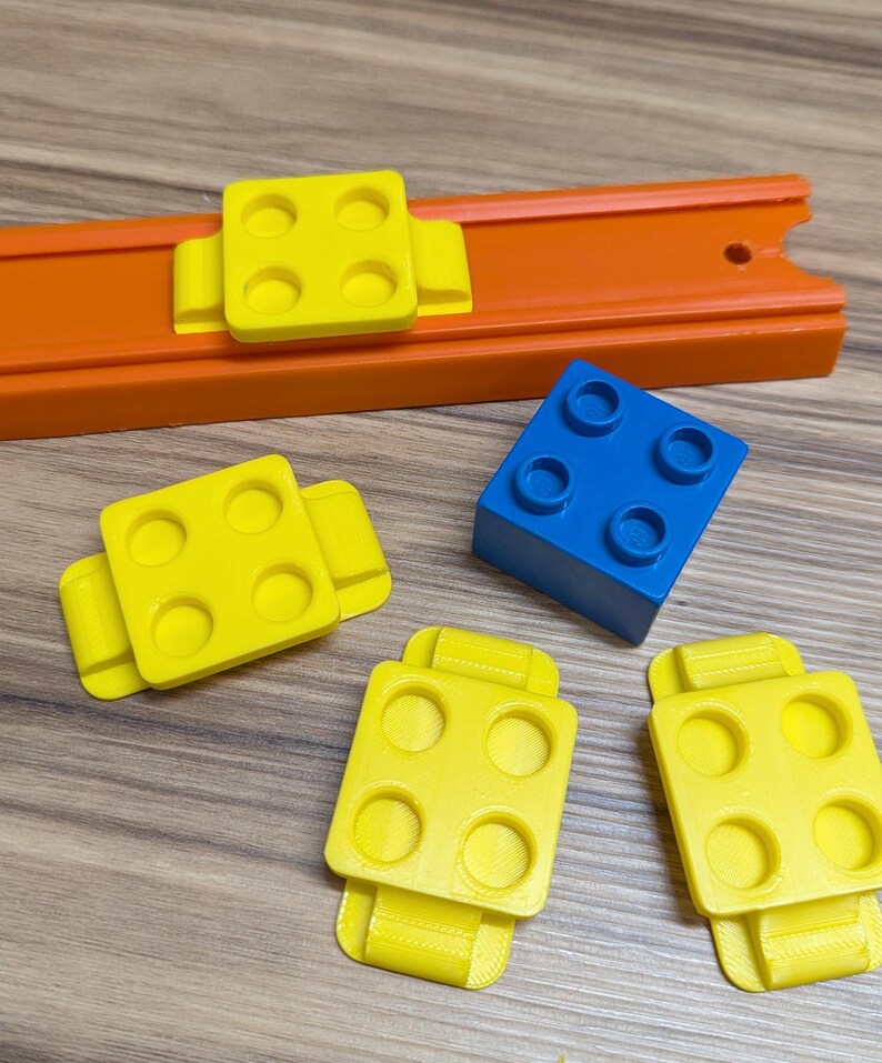 Peut inclure: Quatre pi&egrave;ces en plastique jaune avec quatre trous chacune et un bloc en plastique bleu avec quatre trous. Les pi&egrave;ces jaunes ont une rainure sur le c&ocirc;t&eacute; et sont con&ccedil;ues pour se connecter &agrave; une piste.