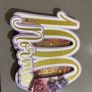 Décoration pour gâteau faite main sur mesure, comprenant du papier cartonné et des paillettes, ainsi que des fleurs en papier cartonné.