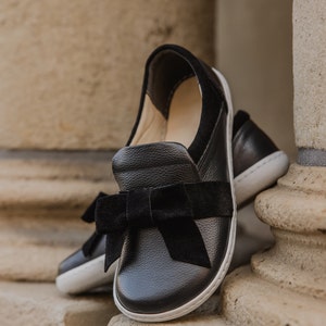 Pode incluir: Sapatos de couro preto com um la&ccedil;o de veludo preto. Os sapatos t&ecirc;m uma sola de borracha branca.