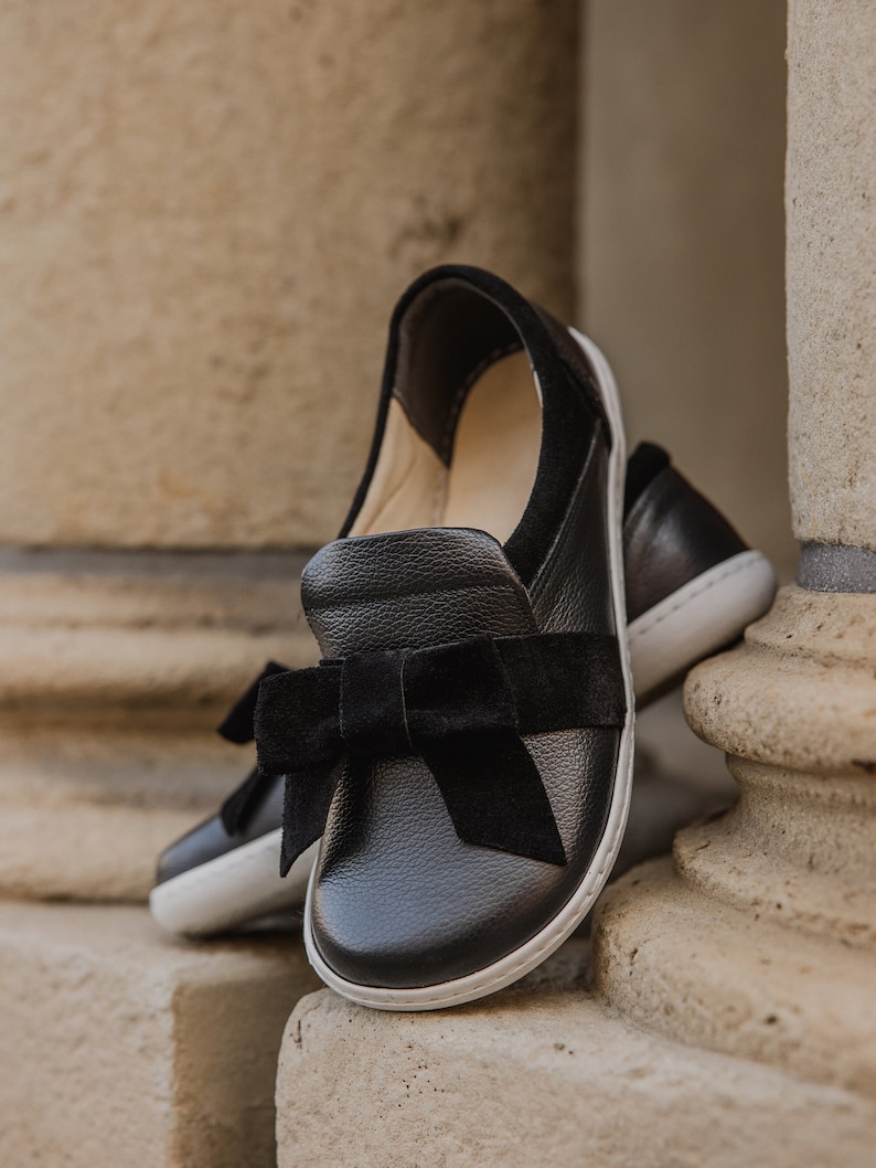 Pode incluir: Sapatos de couro preto com um la&ccedil;o de veludo preto. Os sapatos t&ecirc;m uma sola de borracha branca.