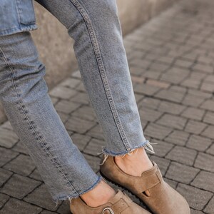 Peut inclure: Une paire de chaussures en daim brun clair avec une boucle. Les chaussures sont port&eacute;es avec un jean bleu clair.