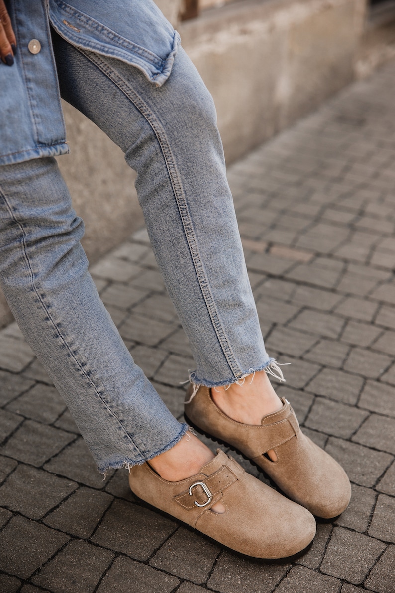 Peut inclure: Une paire de chaussures en daim brun clair avec une boucle. Les chaussures sont port&eacute;es avec un jean bleu clair.