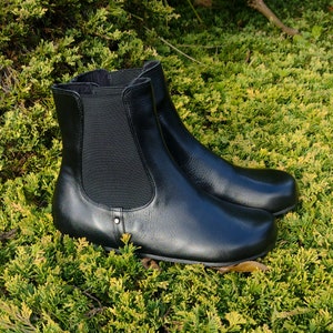 Puede incluir: Un par de botines de cuero negro con paneles laterales elásticos. Los botines tienen una punta puntiaguda y un tacón bajo.