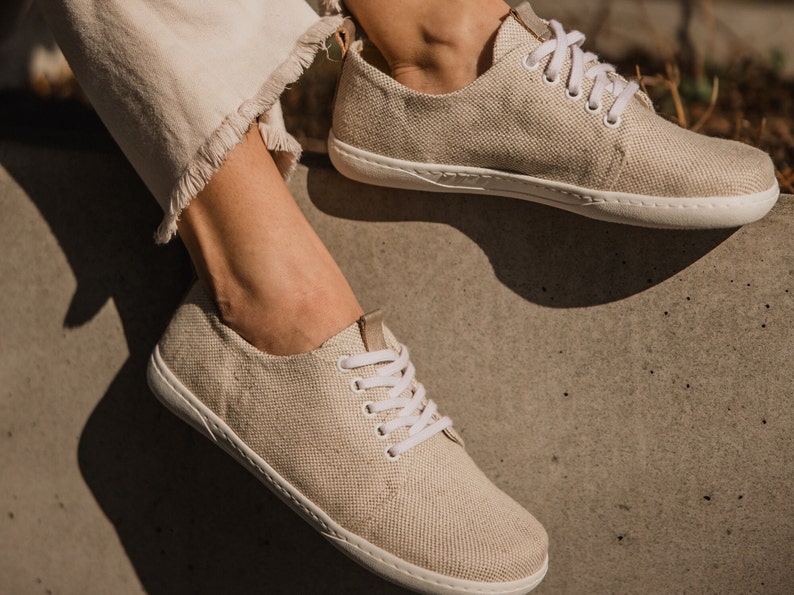 May include: A pair of beige canvas sneakers with white laces. The sneakers have a simple design and are made of a natural material.