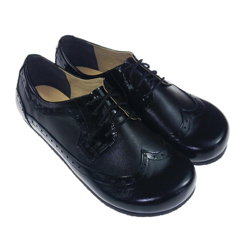 May include: A pair of black leather lace-up shoes with wingtip detailing. The shoes have a rounded toe and a low heel.