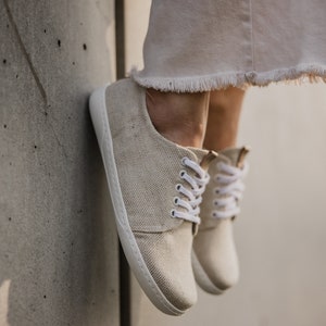 May include: A pair of beige canvas low-top sneakers with white laces. The shoes are worn and have a casual, relaxed look.
