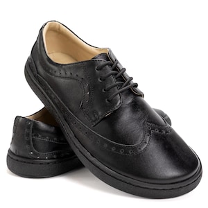 Puede incluir: Un par de zapatos Oxford de cuero negro. Estos zapatos cl&aacute;sicos tienen cierre de cordones y perforaciones decorativas. Se muestran sobre un fondo blanco. La suela es negra.
