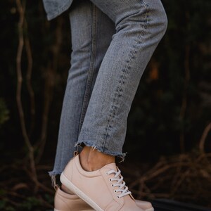 May include: A pair of light pink leather sneakers with white laces. The sneakers are on a black and brown striped surface.