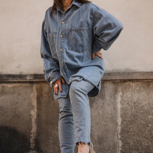 Peut inclure: Une femme portant une chemise en jean bleu clair et un jean avec une paire de chaussures en daim marron &agrave; boucles.