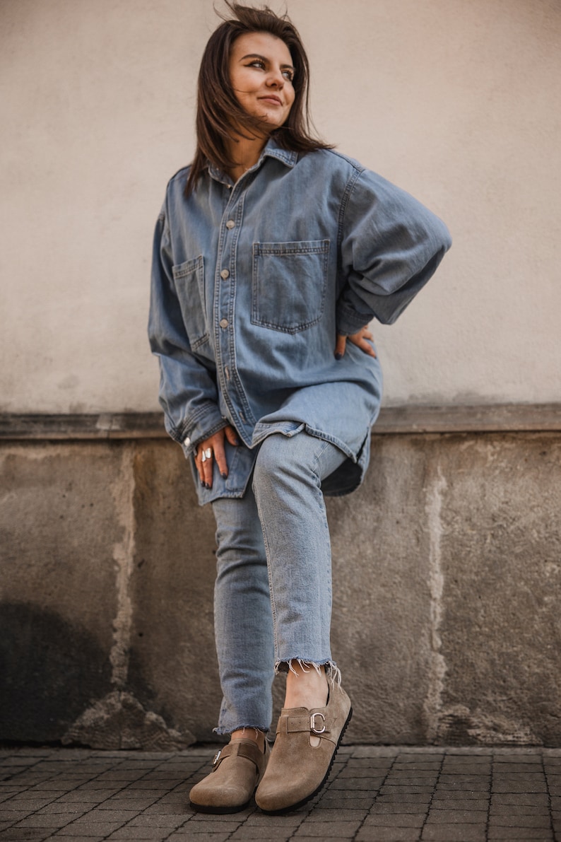 Peut inclure: Une femme portant une chemise en jean bleu clair et un jean avec une paire de chaussures en daim marron &agrave; boucles.