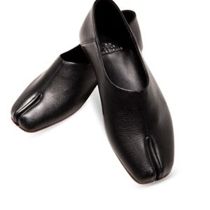 May include: A pair of black leather split-toe flats. The shoes have a rounded vamp and a split between the big toe and the other toes. The shoes are made of a textured leather material.