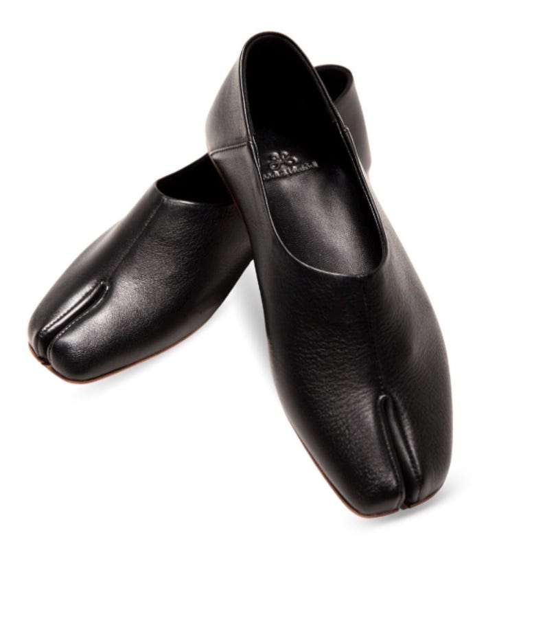 May include: A pair of black leather split-toe flats. The shoes have a rounded vamp and a split between the big toe and the other toes. The shoes are made of a textured leather material.