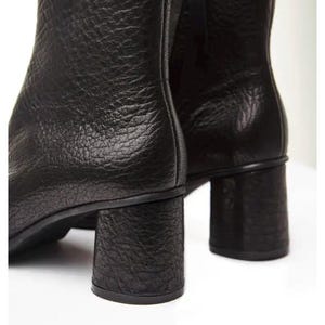 May include: Close-up of two black leather ankle boots. The boots have a textured surface and a chunky, block heel. The heels appear to be approximately 7.6 cm tall. The boots are set against a white background.