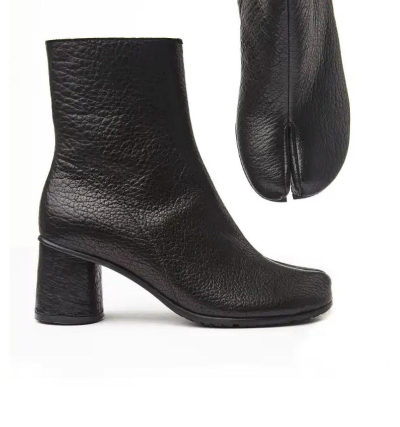 May include: Black leather ankle boots with a split-toe design, featuring a textured surface and a block heel. The boots have a rounded toe and a heel height of approximately 6.35 cm.
