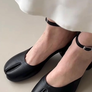 May include: Black leather split-toe shoes with a small heel and ankle strap. The shoes have a unique design with a separate section for the big toe. The ankle straps have a small silver buckle.