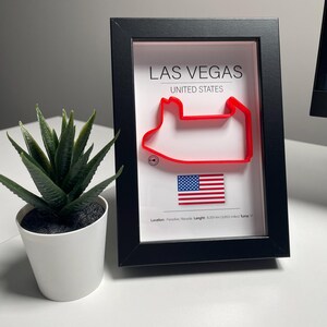 Peut inclure: Une impression encadrée noire de la piste de course du Las Vegas Motor Speedway en rouge avec un petit drapeau américain dans le coin inférieur droit. Le texte "Las Vegas, États-Unis" est imprimé au-dessus de la piste. Le texte "Emplacement : Paradise, Nevada. Longueur : 6,209 km (3,853 miles) Virages : 17" est imprimé sous la piste.