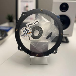 Può includere: Un kit adattatore per altoparlanti audio per auto circolare nero con fori per viti color oro. Il kit include un rotolo di materiale nero e piccole viti nere, confezionate in un sacchetto di plastica trasparente. Il logo "HELIX" e l'adesivo "diecastdonnie" sono visibili.