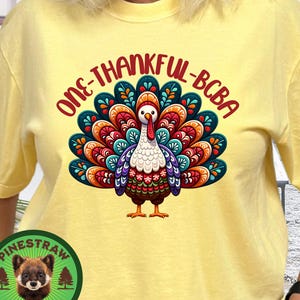 May include: Yellow t-shirt with a colorful turkey graphic and the text "ONE-THANKFUL-BCBA". The turkey has a vibrant tail with red, orange, blue, and green feathers. A round logo with a bear is on the left side.