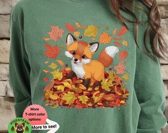 May include: A green long-sleeved t-shirt with a cute cartoon fox surrounded by autumn leaves. The text "More T-shirt color options More to see!" is on the bottom left corner of the shirt.