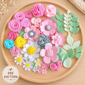 May include: A collection of assorted felt flowers and green leaves in various shades of pink, yellow, blue, and gray arranged on a round wooden tray. A circular label in the bottom left corner features the text PDF PATTERN with a heart icon.