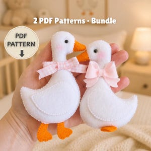 Puede incluir: Dos adornos de fieltro blanco con forma de pato, con picos y patas naranjas, mejillas rosadas y pequeños lazos en el cuello. Un pato lleva un lazo de cuadros vichy rosa y el otro un lazo rosa liso. El texto dice 2 PDF Patterns - Bundle.