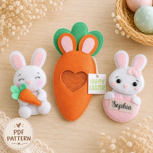Pode incluir: Dois ornamentos de feltro em forma de coelho e um em forma de cenoura com um recorte em forma de coração. Um coelho segura uma pequena cenoura laranja, o outro um coração rosa com o nome Sophia. Uma etiqueta diz HAPPY EASTER.