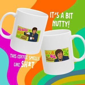 May include: Two white ceramic mugs with humorous cartoon graphics. One mug features a man pouring coffee with the text "This Coffee Smells like SH*T." The other mug has the text "It's a Bit Nutty!" on it.