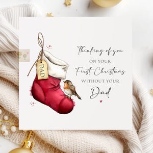 May include: A Christmas card featuring a red stocking with a tag that says "Dad", a small bird, and the text "Thinking of you on your First Christmas without your Dad."