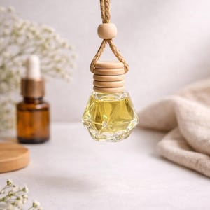 May include: A hanging glass car air freshener bottle with a faceted geometric shape, filled with a pale yellow liquid. The bottle features a light-colored wooden cap and a matching wooden bead, suspended by a thick, braided tan jute rope cord.