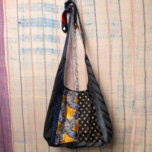 Puede incluir: Un bolso de hombro hecho a mano con corbatas recicladas. El bolso presenta un diseño de patchwork con varios patrones y colores, incluyendo negro, azul, dorado y telas estampadas. Se suspende de una cadena y una corbata.