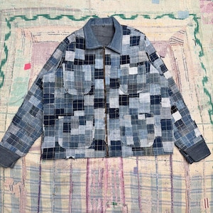 May include: A long-sleeve jacket constructed from a patchwork of various blue denim fabric squares. The garment features a fold-down collar, a full-length front zipper, and four large patch pockets on the front. The cuffs are solid blue denim.