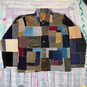 Könnte beinhalten: Eine langärmelige Knopfjacke aus einem Patchwork aus Cordstoffquadraten in verschiedenen Farben wie Braun, Blau, Beige, Burgunderrot und Schwarz. Das Kleidungsstück verfügt über einen klassischen Kragen, eine Knopfleiste auf der Vorderseite und zwei Taschen.