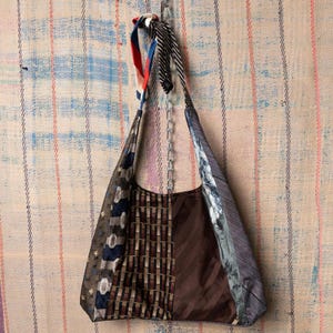 Puede incluir: Un bolso de hombro patchwork hecho de corbatas recicladas. El bolso presenta una variedad de patrones y colores, incluyendo diseños marrones, azules y a rayas. Una cadena plateada y correas de tela de corbata forman la correa para el hombro.