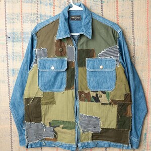 May include: A patchwork denim jacket with a light blue denim collar and sleeves. The front features a variety of fabric patches in shades of green, brown, and camouflage, with two chest pockets. The jacket has a full zipper closure.
