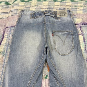 Puede incluir: Vaqueros de mezclilla azul claro con un diseño trasero único que incluye una correa horizontal en la cintura, un bolsillo grande con costura en forma de V y una etiqueta de Levi's Engineered Jeans fechada en junio de 1999 en el lado derecho.