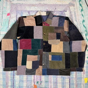 May include: A patchwork corduroy jacket in a variety of colors including black, green, blue, tan, and purple. The jacket has a button-up front, a collar, and long sleeves. The jacket is made of corduroy fabric.