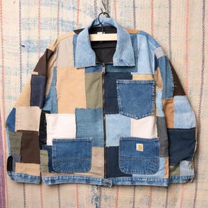 Peut inclure: Veste patchwork composée de divers morceaux de denim et de tissu dans des tons de bleu, beige et marron. La veste est dotée d'un col, d'une fermeture éclair et de deux poches avant. Un petit logo Carhartt est visible sur l'une des poches.