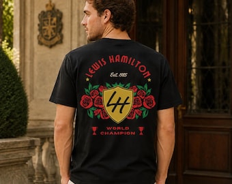 May include: A black short-sleeve t-shirt featuring a back graphic with the text Lewis Hamilton, Est. 1985, and World Champion. The design includes a gold shield with the letters LH, surrounded by red roses and green leaves, with two small trophies.