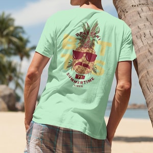 Può includere: Una maglietta verde chiaro con un ananas che indossa occhiali da sole e baffi. L'ananas è circondato dal testo "Summertime Vibes".