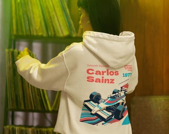May include: A white hoodie featuring a graphic of a Formula 1 race car and the text "Carlos Sainz 1977." The back of the hoodie also has the words "Smooth Operator" and other text. The design incorporates red, blue, and teal colors.